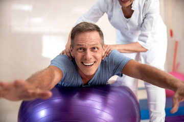 Fototapeta na wymiar Smiling man doing exercises on a fintes ball