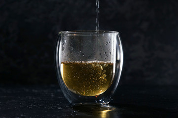 Hot green tea is pouring in a glass cup on a black background, tea ceremony.