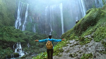 Woman enjoying view on the waterfall Tumpak Sewu and raises her hands up, Java island, Indonesia