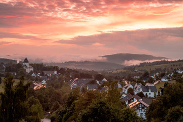 Dramatic sunset view over the mountainous village of Grafschaft in the winter sports region of Sauerland, Germany, with a colourful orange lit cloudy sky
