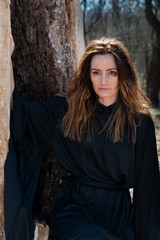 Young  tall Woman with dark long hair in black robes deep in the Forest. Witches. Halloween and Gothic concept. Witchcraft and magic. 