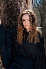 Naklejka premium Young tall Woman with dark long hair in black robes deep in the Forest. Witches. Halloween and Gothic concept. Witchcraft and magic. 