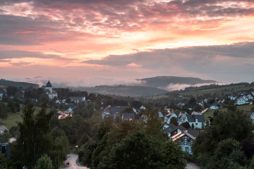 Mountainous village of Grafschaft in the winter sports region of Sauerland, Germany, during a colourful orange lit cloudy sky at sunset