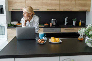 Happy adult woman is looking away in the kitchen