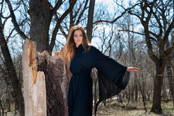 Young  tall Woman with dark long hair in black robes deep in the Forest. Witches. Halloween and Gothic concept. Witchcraft and magic. 