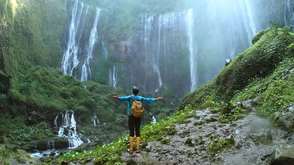 Woman enjoying view on the waterfall Tumpak Sewu and raises her hands up, Java island, Indonesia