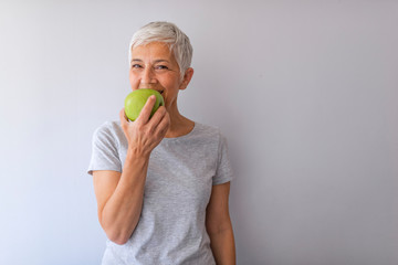 Portrait of happy mature woman holding granny smith apple at home. Beautiful senior woman over...