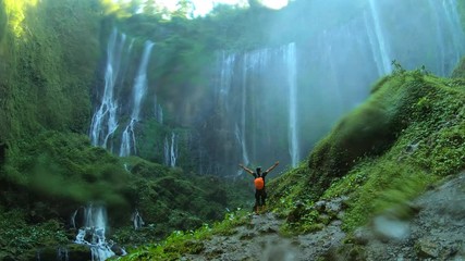Tourist walks through the waterfall ,  and raises her hands up, enjoying view on the waterfall Tumpak Sewu in Java island, Indonesia