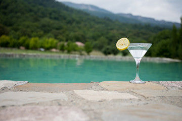 Glass of martini cocktail at swimming pool with ocean and palm tree background. A glass of blue martini cocktail welcome drink bar.Selective focus. season and holidays concept.