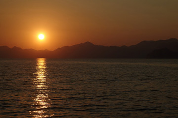 Naklejka premium View from the yacht to the sun setting behind the mountains