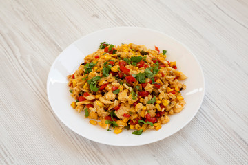 Homemade southwestern egg scramble on a white plate on a white wooden background, side view.