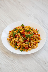 Homemade southwestern egg scramble on a white plate on a white wooden surface, side view. Close-up.