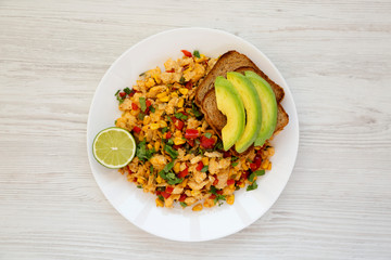 Homemade southwestern egg scramble with toast on a white plate on a white wooden table. Flat lay, overhead, from above. Close-up.