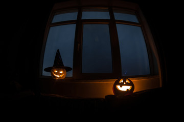 Scary Halloween pumpkin in the mystical house window at night or halloween pumpkin in night on room with blue window. Symbol of halloween in window.