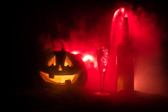 Two glasses of wine and bottle with Halloween - old jack-o-lantern on dark toned foggy background. Scary Halloween pumpkin