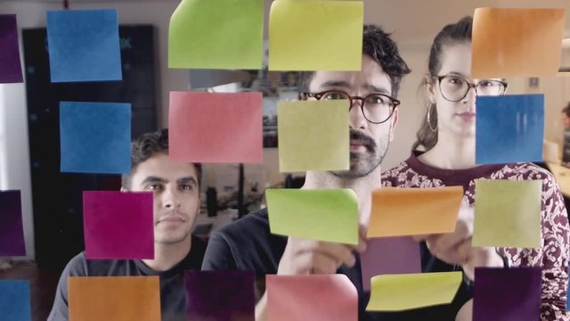 Creative development team brainstorms on glass whiteboard covered in sticky notes