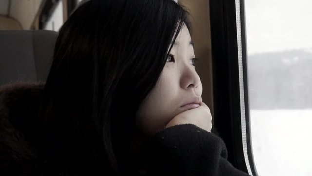 Asian Girl looking out of moving train window at wintery snow landscape