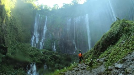 Tourist walks through the waterfall ,  and raises her hands up, enjoying view on the waterfall Tumpak Sewu in Java island, Indonesia