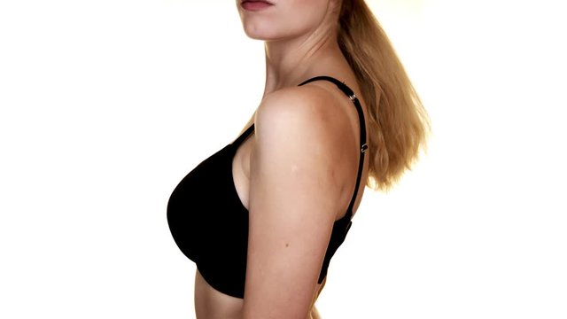 A woman turned to the side, wearing a black bra, in front of a white studio backdrop