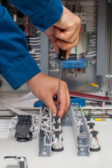 Hands of electrician with screwdriver tighten up switching electric actuator equipment in fuse box