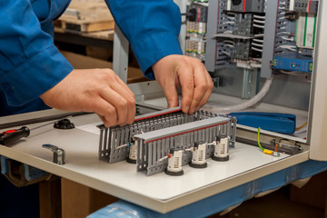 Hands of electrician with screwdriver tighten up switching electric actuator equipment in fuse box