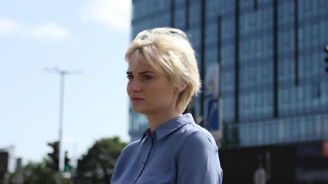 Sad blond girl stands lonely alone outside on the street. Her hairs blows in the wind. Close up shot.