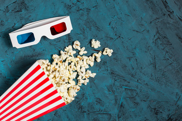 Popcorn bucket and 3D glasses with copy space on blue textured background. Top view. Flat lay