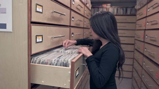 young woman in music library, searching drawers with compact discs