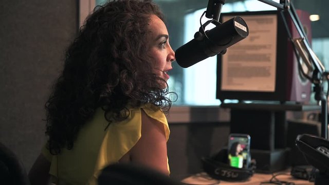 beautiful young female speaker with curly hair speaking into the microphone for the live radio show