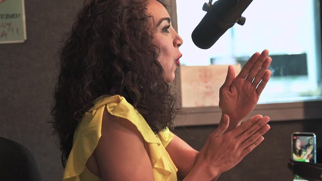 beautiful young female speaker with curly hair speaking into the microphone for the live radio show and gesticulating with hands