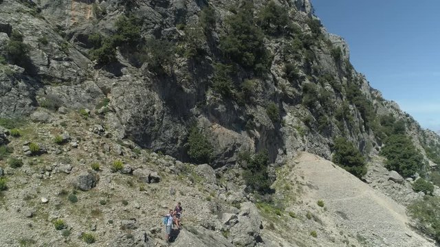 Aerial dronie shot of three people staying on a rock of the hiking trail path to gola gorropu on sardinia