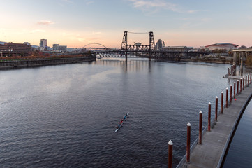 Willamette River at sunset with rowers in a boat in the foreground, Fremont, Broadway, and Steel...