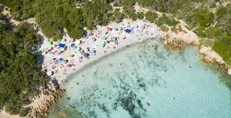 View from above, stunning aerial view of a beautiful beach full of colored beach umbrellas and people swimming in a turquoise clear water. Capriccioli Beach,Sardinia, Italy.