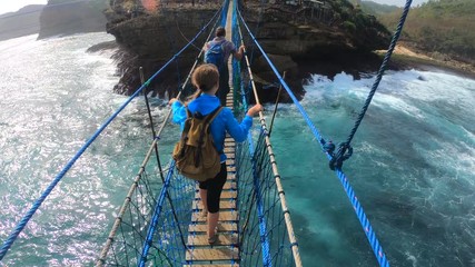 PoV action camera - people go on suspension bridge above ocean waves in Timang beach, Java island, Indonesia