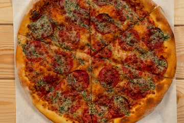 Salami pizza with basil sauce on wooden background - Top view