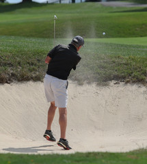 A golfer jumps as he hits out of a sand bunker