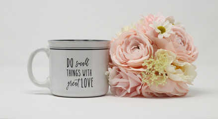 inspirational love message on a white and grey coffee mug next to a pastel bouquet of flowers on a white background