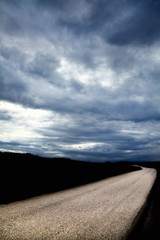 empty countryside single lane road over dramatic sky with storm clouds