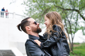 Fototapeta premium Fashionable stylish family for a walk. Daughter in the hands of dad. Happiness being a parent. Unconditional love. Time together. Family look. Urban casual outfit. 