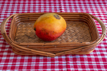 A mango fruit on a basket over a red and white checkered cloth 
