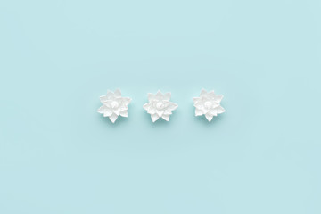 Decorative wax white candles - lotus flowers on pastel blue background. Minimalistic spa composition. Flat, lay, top, view.