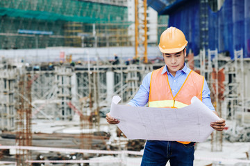 Obraz na płótnie Canvas Serious professional Asian civil engineer examining building plan at working area