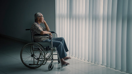 Senior man sits in the wheelchair near the window