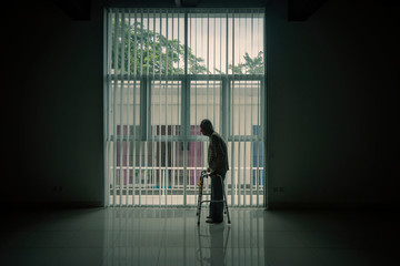 Fototapeta na wymiar Silhouette of old man walks near the window