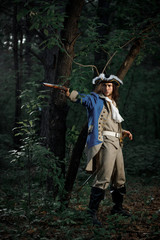 18th-century officer with flintlock gun stands by tree in forest