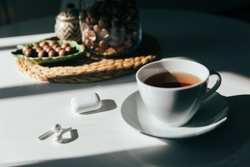 Macadamia nuts in a bowl, cup of tea or coffee and earphones lay in the kitchen table, hard morning light