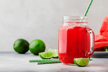 Freshly squeezed watermelon smoothie with lime in glass jar and slices of watermelon on gray kitchen table background