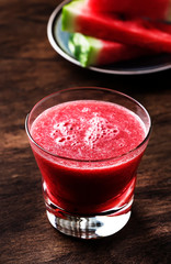 Freshly squeezed watermelon smoothie in glass and slices of watermelon on old wooden kitchen table background