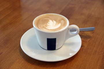 Cappuccino with milk-foam decoration in a white cup on a wooden table