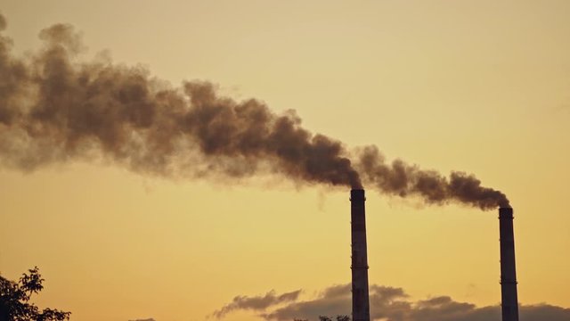 Dark smoke comes from large pipes into the air on the evening sky background. Dirty emissions pollute the environment. Ecological problems in the air.